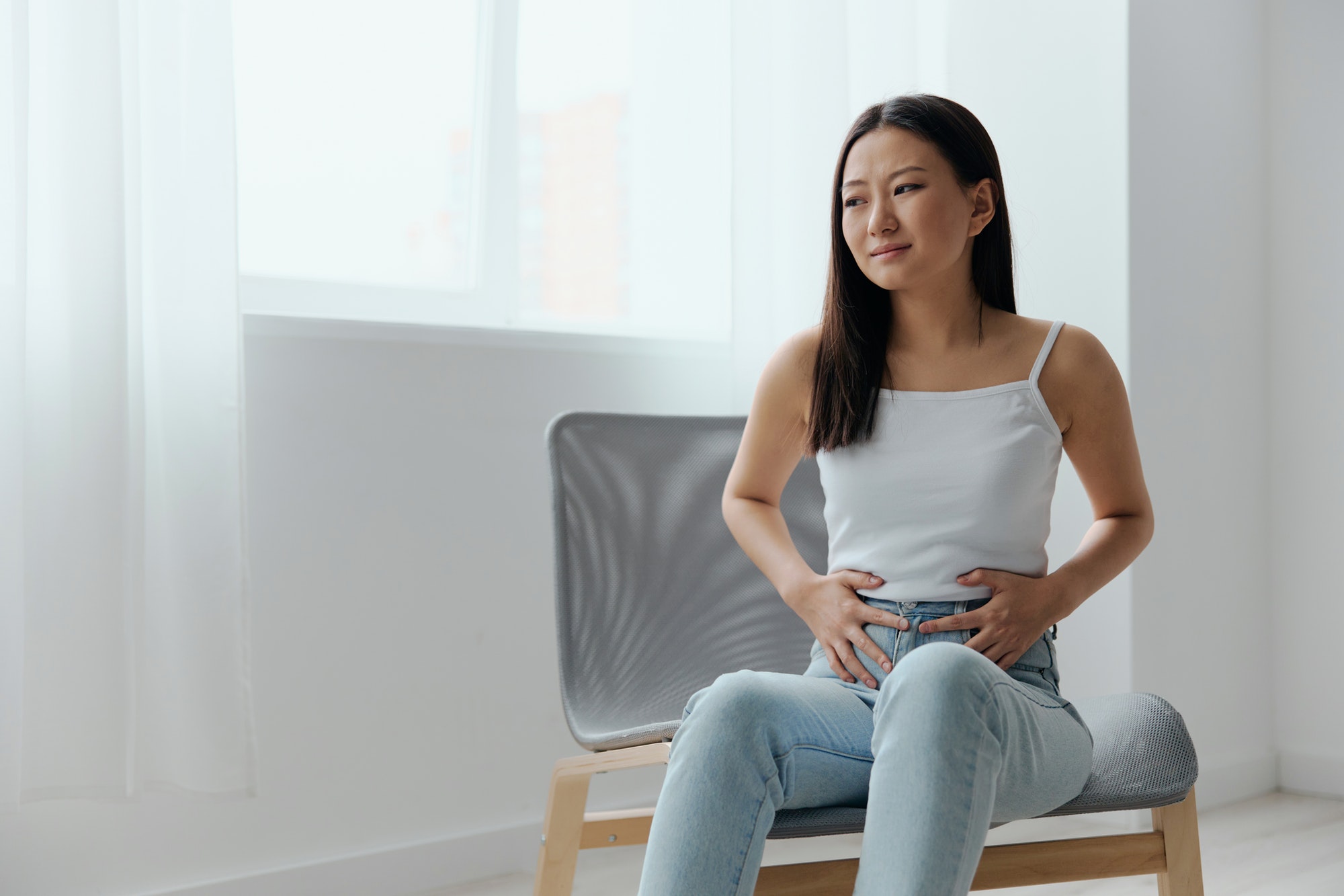 Stomach ulcer Gastritis. Tormented suffering tanned beautiful young Asian woman hold hands on